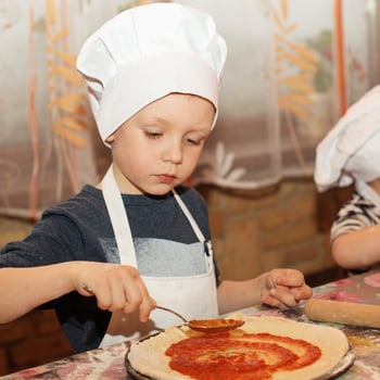 A little boy making his own pizza.