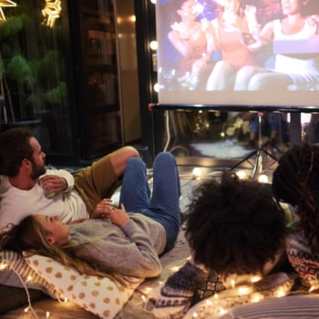 A family watching a movie together surrounded by Christmas lights.