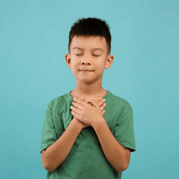 A little boy with eyes closed holding his hands over his chest as a way to show gratitude.