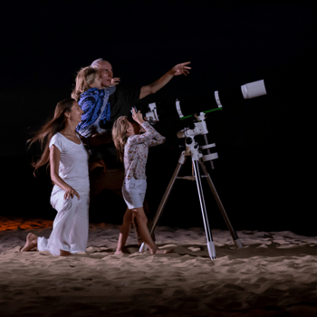 A family star gazing with a telescope on the beach.