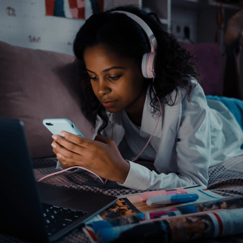 A girl listening to music on her phone in her bed.