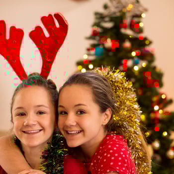 Two kids smiling together for a photo in front of a Christmas tree.