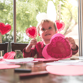 A little boy holding up a heart shaped doily craft.