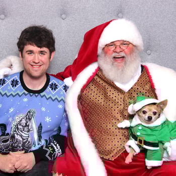 A chihuahua dressed in an elf outfit with his owner and Santa.