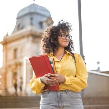 A girl standing with school books in front of her school.