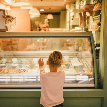 A little girl looking into a case of ice cream at an ice cream shop.