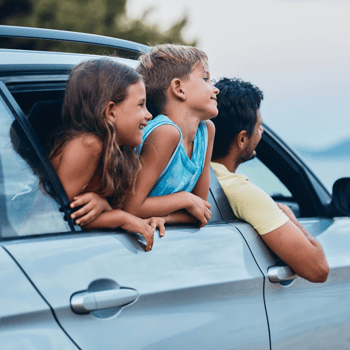 Two kids and their dad leaning out of a car window looking out.