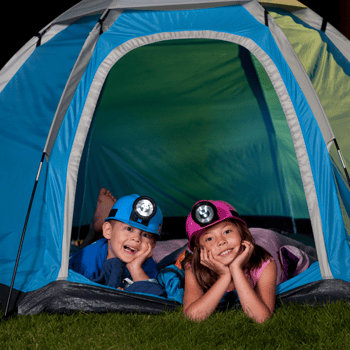 Two kids in a tent with head lights on.