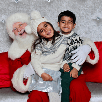 A little boy and girl sitting with Santa and smiling.