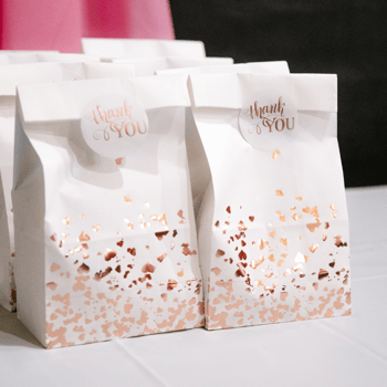 Goodie bags that are white with gold hearts on the bottom with a sticker that say "thank you!"