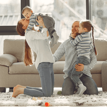 A mom kissing her baby on the cheek while a dad holds their toddler.