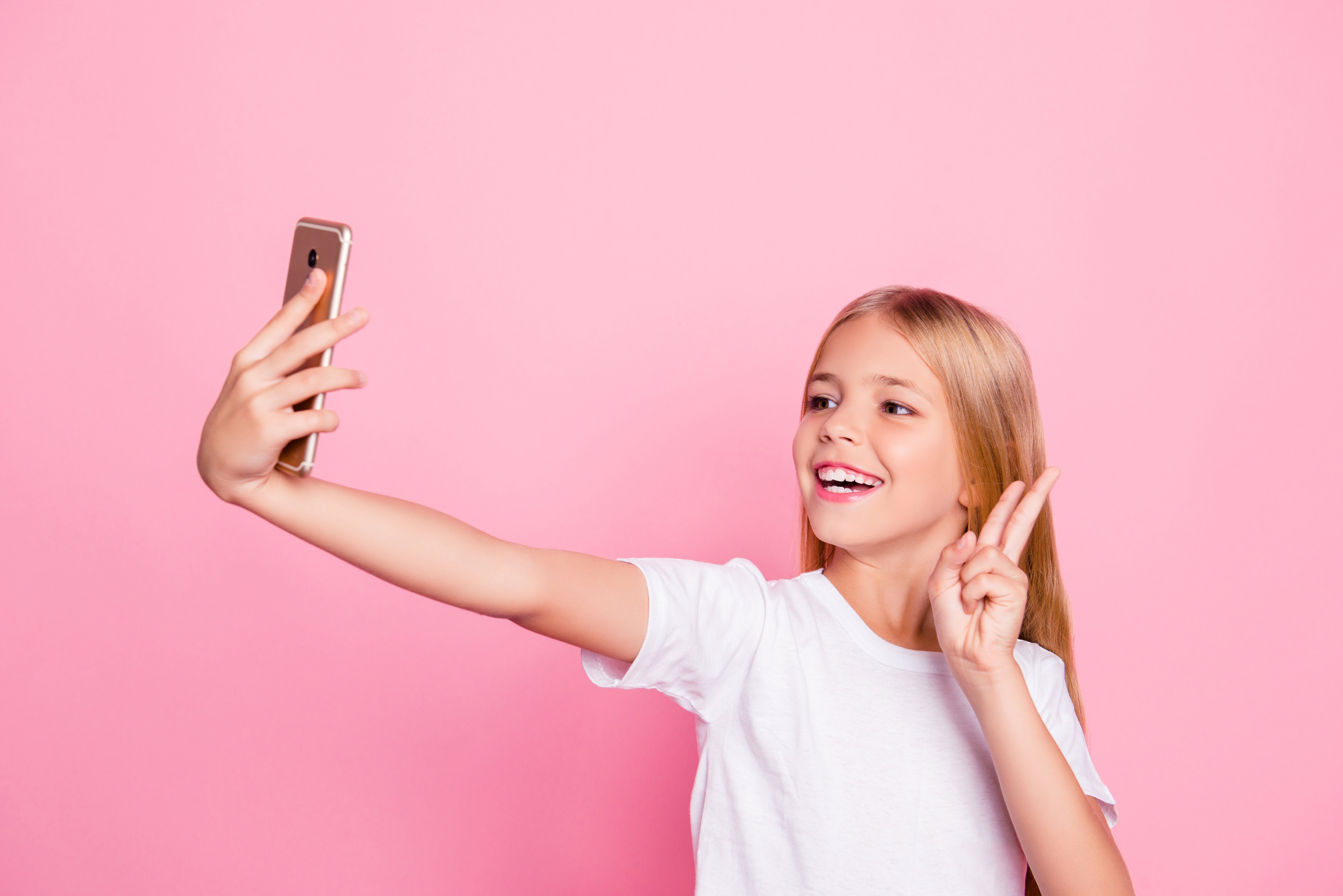 young girl holding phone and making peace sign to take selfie with cell phone