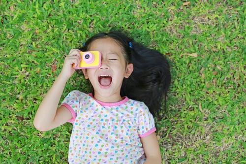 Little girl laying in grass with camera