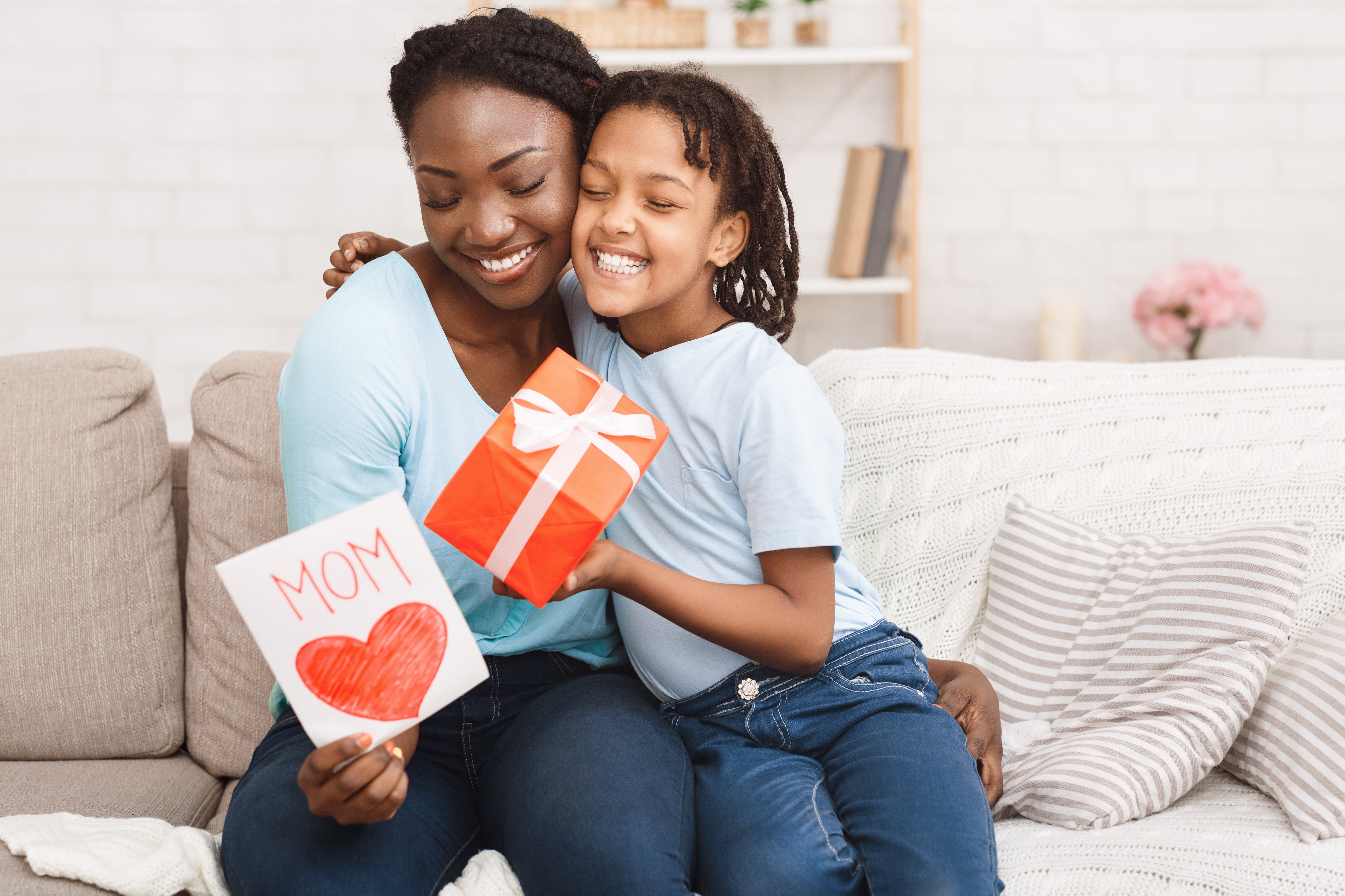 mother-and-daughter-sitting-on-couch-celebrating-mothers-day-exchanging-card-and-gift