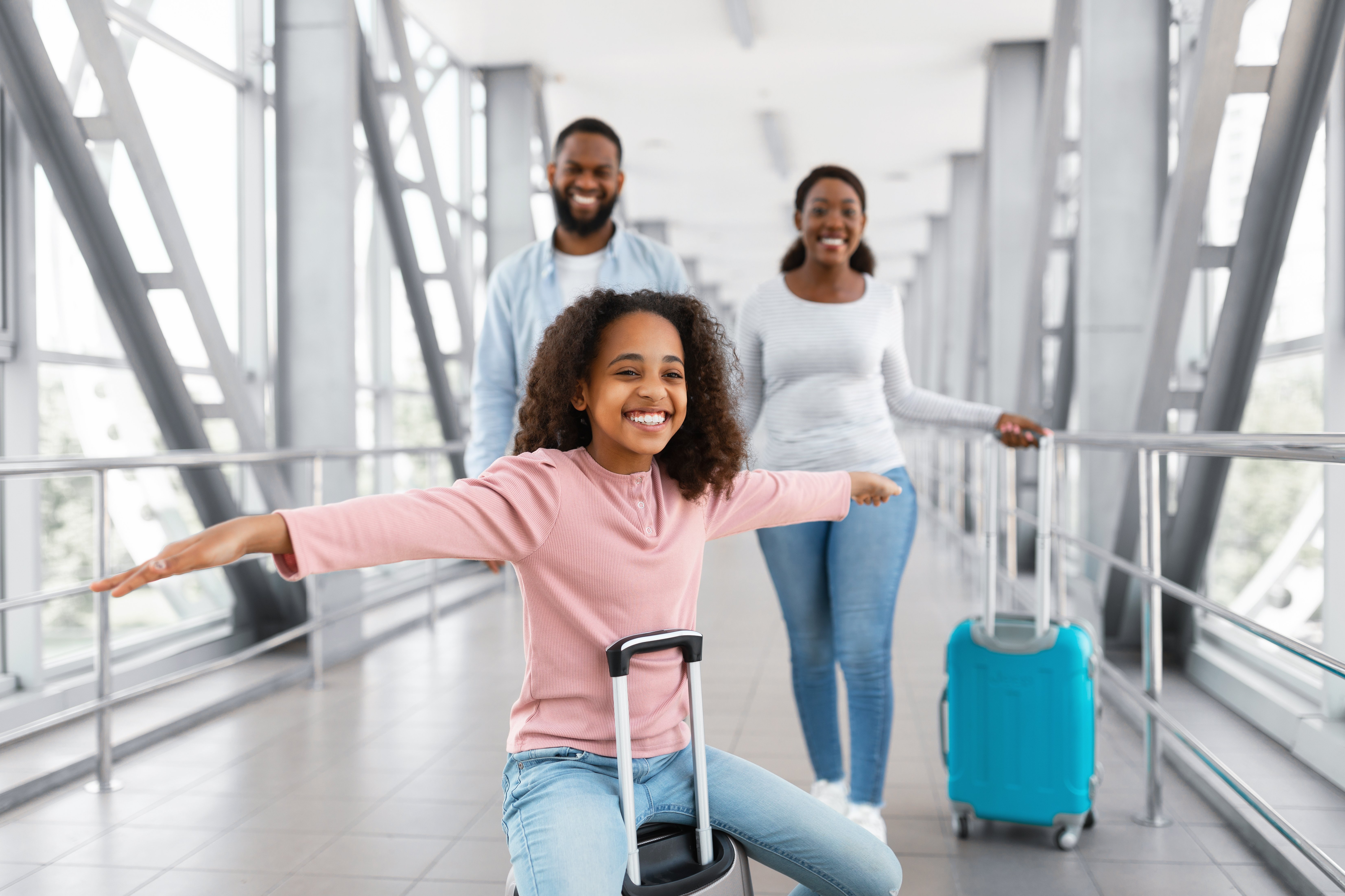 family traveling in airport with girl sitting on suitcase