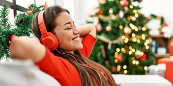 smiling woman in sweater with headphones on sitting in living room with christmas tree in the background