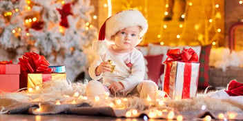 Baby with Santa hat sitting in front of tree on Christmas day surrounded by presents