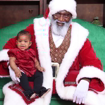 Black Santa with a baby girl in a red dress.