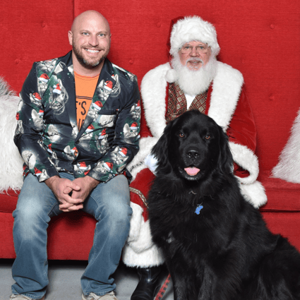 A black dog with their owner next to Santa.