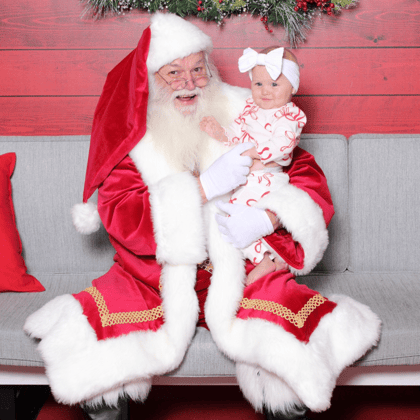 A happy baby girl in festive outfit smiling with Santa.