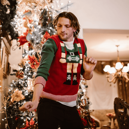 A guy in a christmas sweater dancing by the tree.