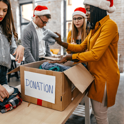 Group of people wearing Santa hats putting together a donation box.