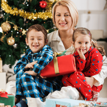 A mom with her kids sitting by the Christmas tree with presents.