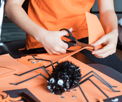 A girl cutting a piece of orange foam for a halloween craft.