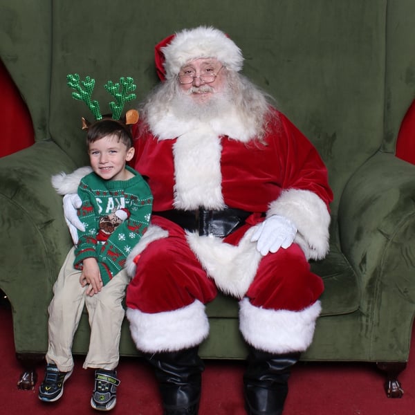 Little boy with Christmas sweater and antlers sitting with Santa during a sensory friendly event