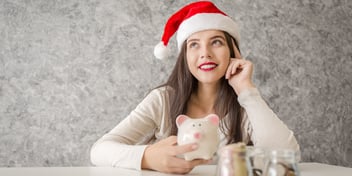 woman wearing santa hat saving money in a piggy bank for the holidays