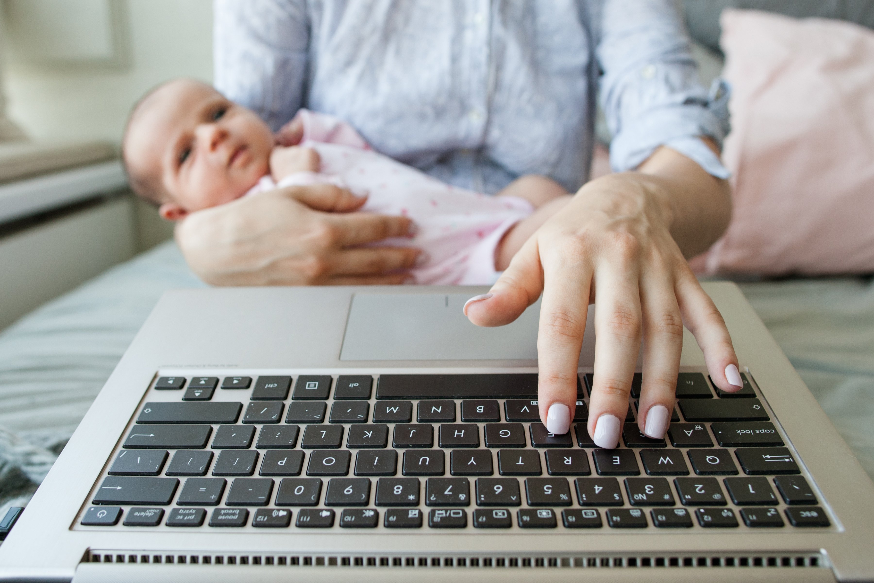 mother with newborn baby typing on laptop computer