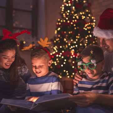 Family reading a christmas book around a christmas tree.