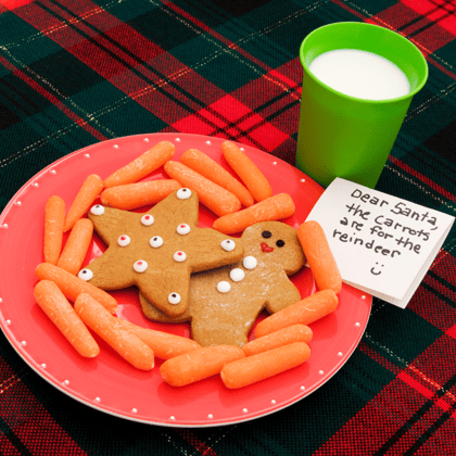 A plate with cookies and carrots with a cup of milk and a note for Santa.