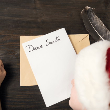 Little boy in Santa hat writing a letter to Santa.