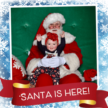 A little girl sitting with Santa with her hands up;