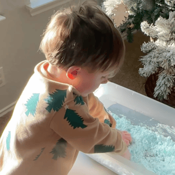 Little boy playing in the bin of fake snow.