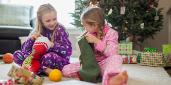 two girls opening stockings to find presents on Christmas by the tree