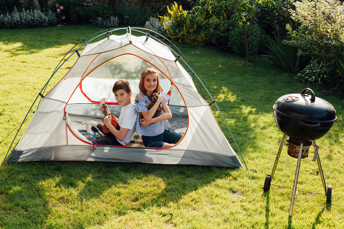 boy-playing-ukulele-sitting-back-back-his-sister-tent-near-barbecue-grill