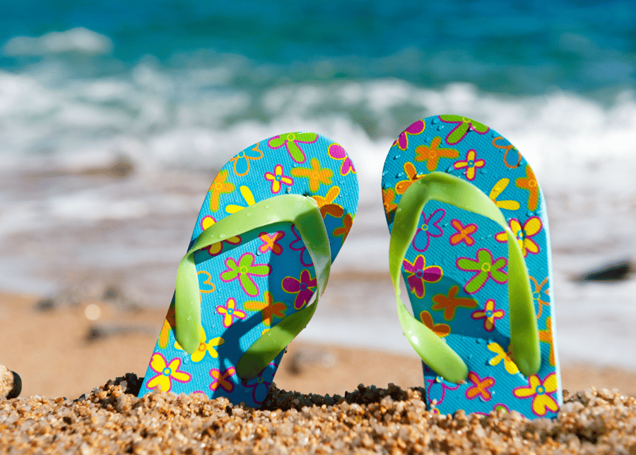 colorful flip flops sticking out of sand on the beach