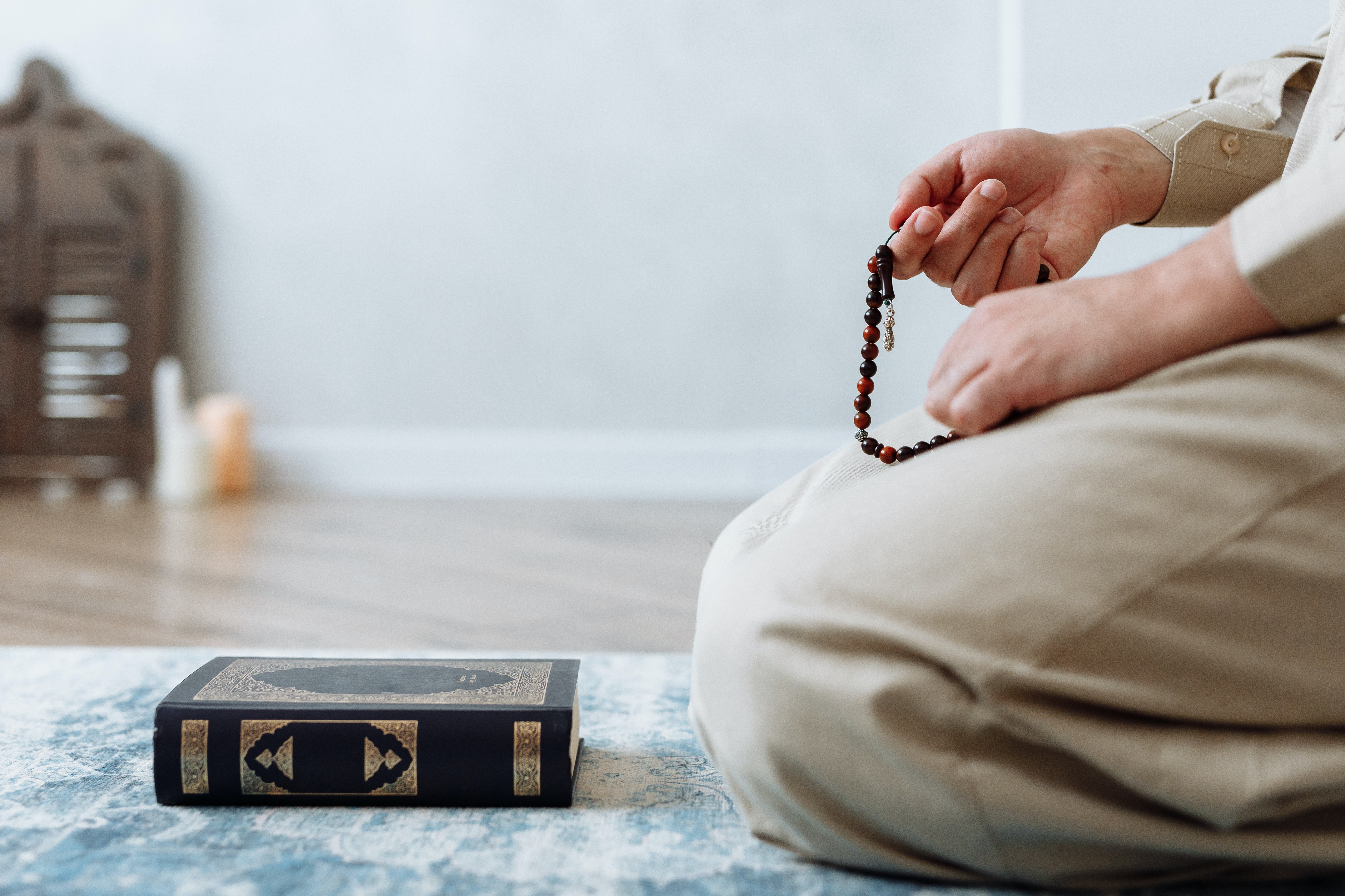 person-kneeling-on-prayer-rug-with-prayer-beads-and-quran-koran-praying
