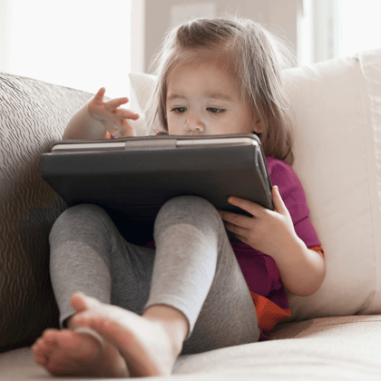 Toddler having some quiet time alone on the couch playing with a tablet.