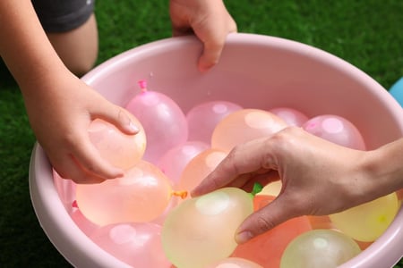 woman and little boy taking water balloons from pile
